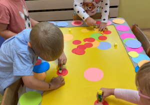 naklejanie przez dzieci kolorowych kół na wielką ramkę