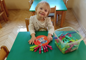 Dziewczynka ozdabiająca papierowy talerz klamerkami.