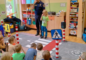 Strażnik miejski i chłopiec, pokazują dzieciom jak zapamiętać numer 112 pokazując go na swojej buzi.