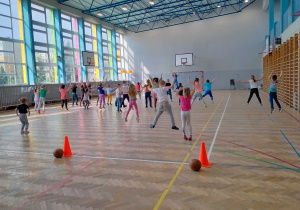 Dzieci podskakują przy piosence i powtarzają ruchy pokazywane przez instruktorkę.