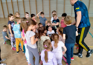 Dzieci siedzą w grupie i słuchają trenera sportowego.