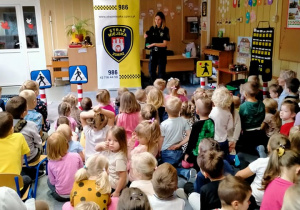 Strażniczka Miejska pokazuje dzieciom zielone światło na sygnalizacji świetlnej.