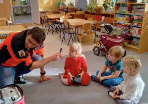 Ratownik medyczny omawia dzieciom sprzęty znajdujące się w torbie ratunkowej.