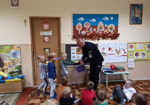 Dzieci wręczją panu policjantowi pamiątkowy upominek.